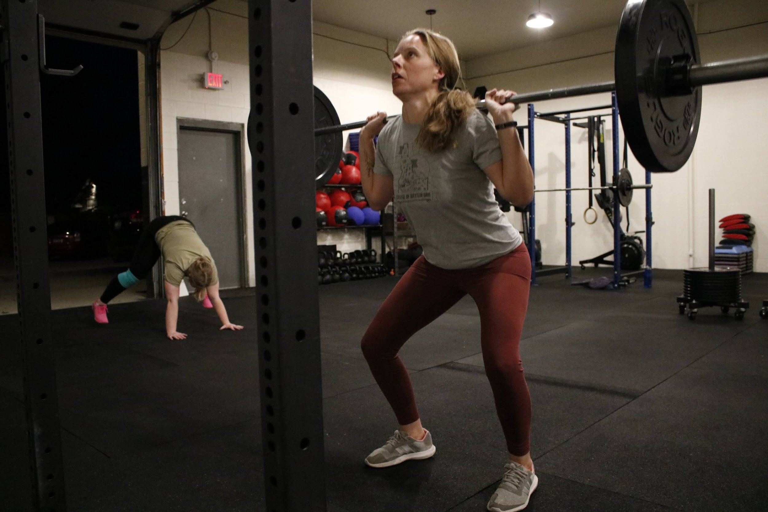 Woman in gray T-shirt and red leggings performing a barbell squat at a gym